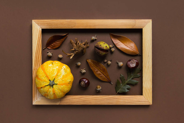 Autumn composition made of pumpkins, dried leaves, chestnuts and acorns in a wooden frame on brown background. Autumn, fall, halloween concept. Flat lay, top view, copy space - Fotoğraf, Görsel
