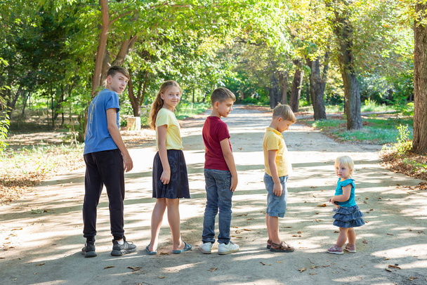 Cinq enfants se tiennent en rangée dans le parc, marchant et se relaxant dans la nature. - Photo, image