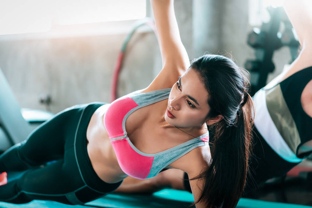 Femme sportive fait bordure latérale pour entraîner ses abdominaux avec entraîneur de fitness masculin dans la salle de gym. - Photo, image