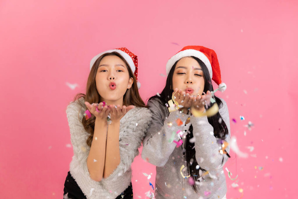 Portrait of two lovely cute asian women in christmas hats  looking at camera isolated over pink background.Attractive asian woman smile in christmas, new year, valentine day, birthday celebration concept. - Foto, Imagem