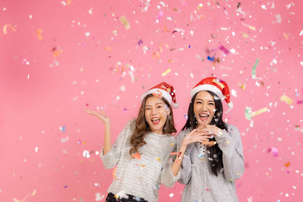 Portrait of two lovely cute asian women in christmas hats  looking at camera isolated over pink background.Attractive asian woman smile in christmas, new year, valentine day, birthday celebration concept. - Foto, immagini