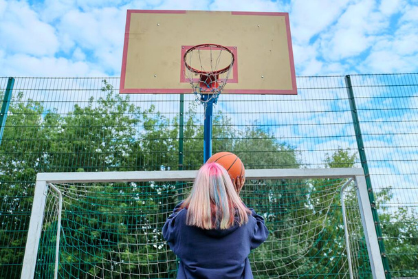 Teenager girl jumping with ball playing street basketball, back view - Fotoğraf, Görsel