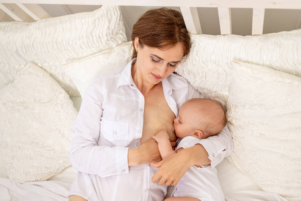 mamá amamantar bebé 6 meses de edad acostado en una cama blanca, alimentación del bebé, lugar para el texto - Foto, imagen