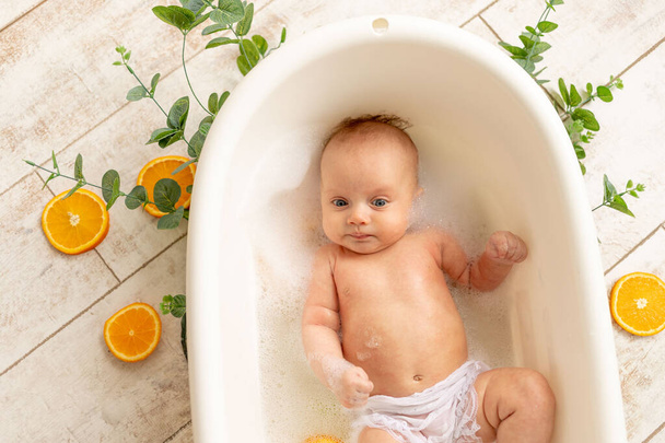 een klein kind baadt in een bad met schuim en sinaasappels, kinderen zijn allergisch voor citrus - Foto, afbeelding
