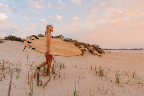 Surfer Mädchen am Sandstrand mit Surfbrett bei warmem Sonnenuntergang oder Sonnenaufgang. Attraktive Surferinnen am Strand - Foto, Bild