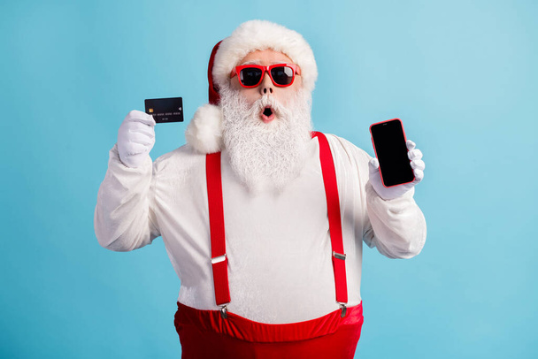 Portrét jeho atraktivní ohromený bělovlasý Santa držení v ruce demonstrující kreditní karty gadget objednat obchod koupit dobrý produkt hotovost zpět izolované světlé zářivý lesk pulzující modrá barva pozadí - Fotografie, Obrázek