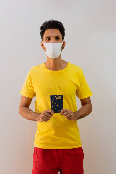 Man black with pandemic mask  holding a Brazilian passport Mercosur, isolated white background - Photo, Image