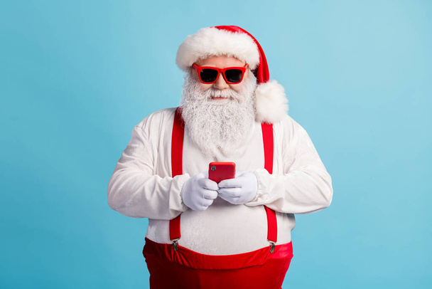 Portrait de son il agréable joyeux joyeux concentré Père Noël aux cheveux blancs en utilisant l'appareil gadget 5g app chat blog boutique ordre isolé lumineux vif éclat vibrant fond de couleur bleue - Photo, image