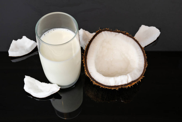 Kokosmilch und getrocknete Kokosnussstücke auf einem verspiegelten schwarzen Hintergrund. - Foto, Bild