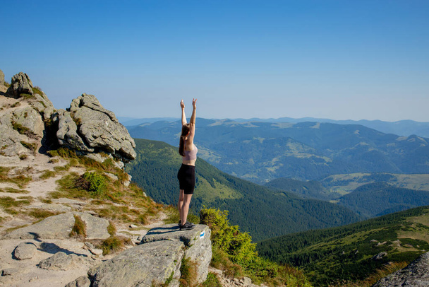 The young Woman at the top of the mountain raised her hands up on blue sky background. The woman climbed to the top and enjoyed her success. Back view. - Photo, image