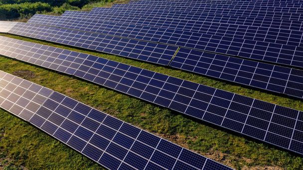 Solar Power Station in Green Field on Sunny day. Aerial view. Solar Panels Stands in a Row in Field for Power Production. Drone fly over Solar Farm. Renewable green energy. Alternative energy sources - Photo, image