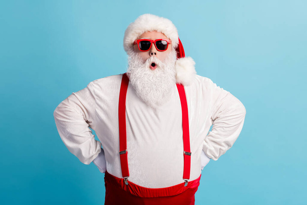 Photo of pensioner old man grey beard hands hips self-assured shock late wake up present delivery wear santa costume red suspenders spectacles white headwear isolated blue color background - Foto, Bild