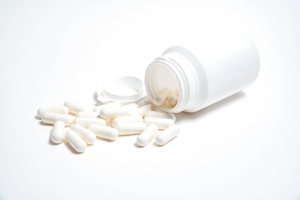 tubo de plástico blanco sin inscripciones de píldoras sobre un fondo blanco y píldoras blancas cerca - Foto, imagen