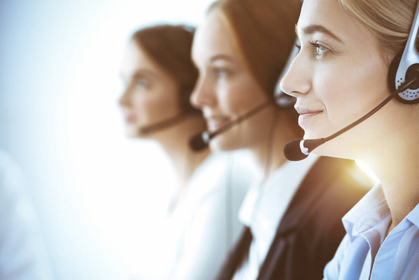 Call center and business people concept. Beautiful business woman with headphones consulting clients. Group of diverse phone operators at work in office - Valokuva, kuva