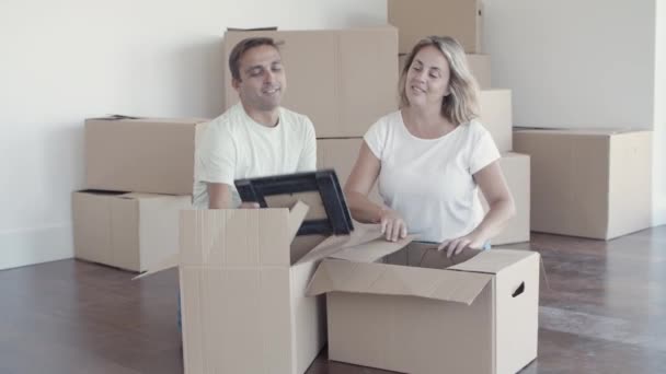Wesoła para rodzinna rozpakowuje rzeczy w nowym mieszkaniu - Materiał filmowy, wideo
