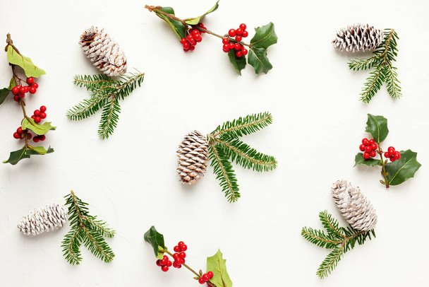 Christmas background with pine cones, branches of holly with red berries and fir tree on white. Winter festive nature concept. Flat lay, copy space. - Fotografie, Obrázek