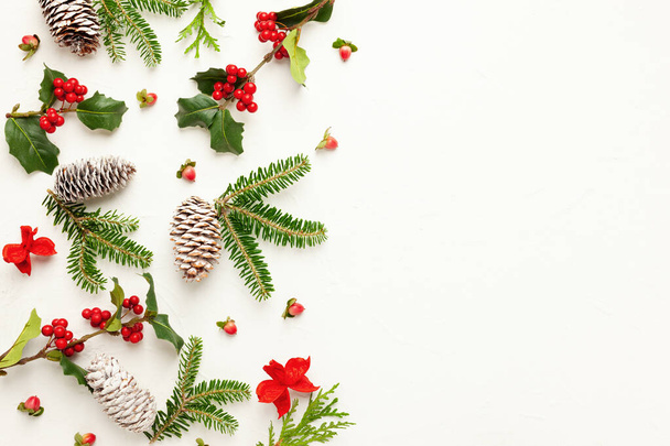 Christmas background with pine cones, branches of holly with red berries and fir tree on white. Winter festive nature concept. Flat lay, copy space. - 写真・画像