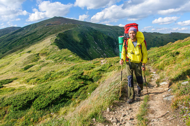 A sports man with a large backpack and trekking poles in his hands walks along a mountain trail in the Carpathian Mountains. Ukraine - Photo, Image
