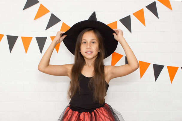 Lustiges lustiges Mädchen mit Hut und Hexenkostüm zu Halloween hält Hüte in der Hand. - Foto, Bild