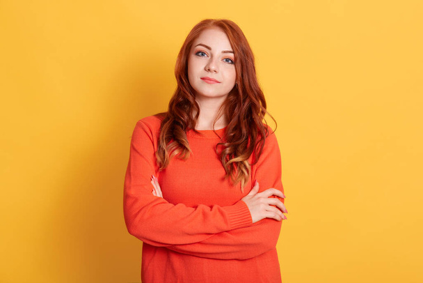 Gorgeous young woman with perfect clean skin wearing casual jumper, has ginger hair, looking at camera, keeping hands folded, posing isolated over yellow background. - Foto, Bild