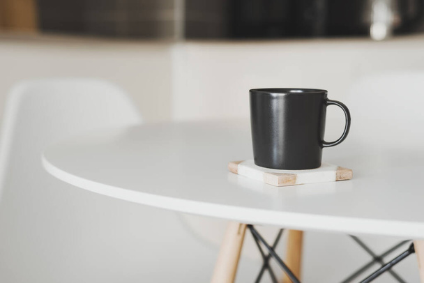 Lege zwarte koffiemok staan op een marmeren onderzetter aan de keukentafel - Foto, afbeelding