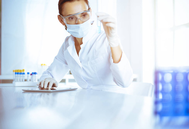 Female laboratory assistant analyzing test tube with blue liquid. Medicine, health care and researching concept - Photo, image