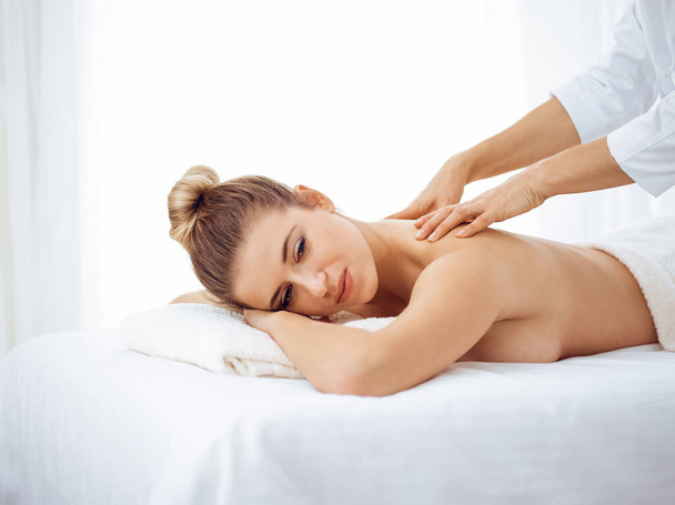Young and blonde woman enjoying massage of back in spa salon. Beauty concept - Foto, Bild