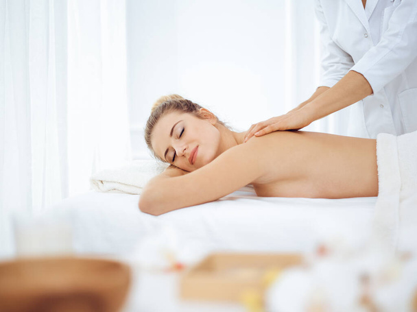 Young and blonde woman enjoying massage of back in spa salon. Beauty concept - Фото, изображение