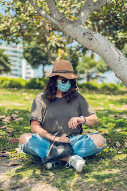 Γυναίκα κοιτάζει το ρολόι της σε εξωτερικούς χώρους και προστατεύει τον εαυτό της με μια ιατρική μάσκα. Νέο φυσιολογικό - Φωτογραφία, εικόνα