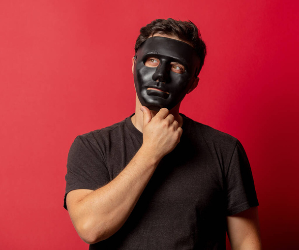 Blanke man met zwart masker op rode achtergrond  - Foto, afbeelding