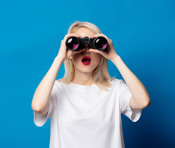 Blonde in white t-shirt with binoculars on blue background - Photo, Image