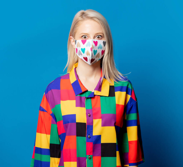 Blonde girl in 90s shirt and face mask on blue background - Photo, image