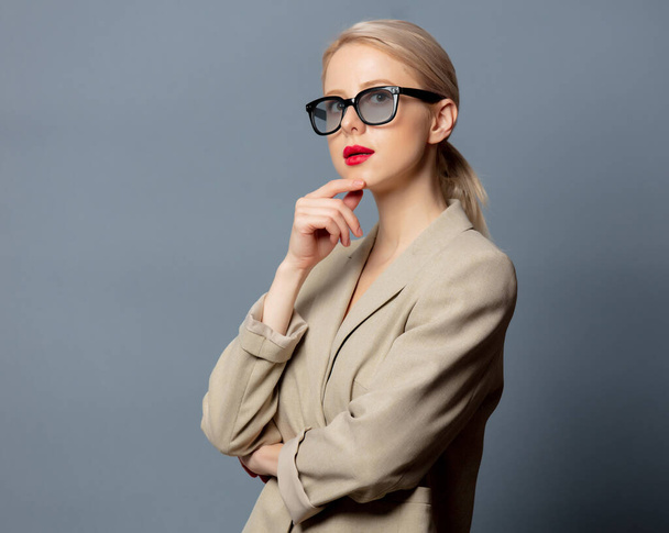 Blonde woman in jacket and glasses on gray background  - Fotografie, Obrázek