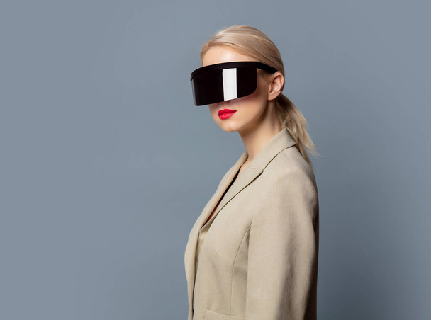 Style blonde in futuristic VR glasses on gray background - Foto, afbeelding