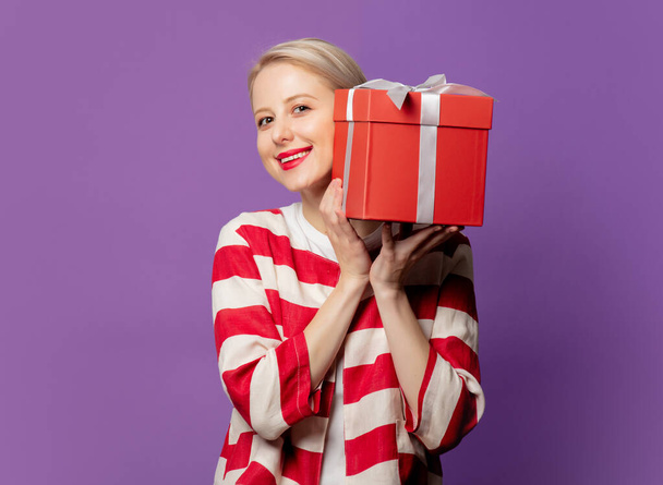 Beautiful blonde in red jacket with gift box on purple background - Фото, зображення