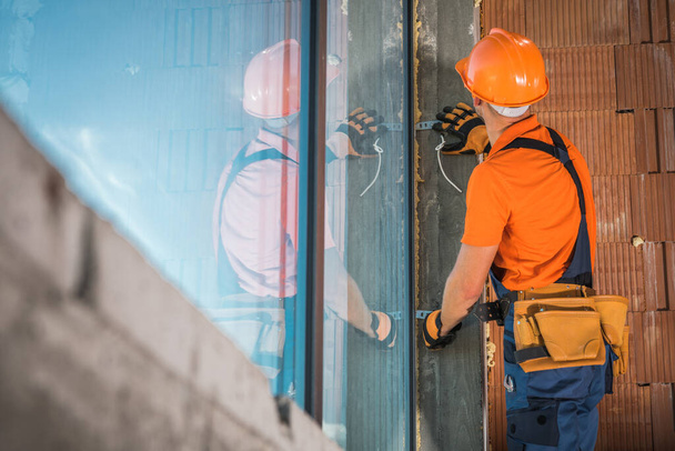 Commerciële Building Windows Installatie door blanke contractant werknemer in zijn veertiger jaren dragen van oranje shirt en harde hoed. Industrieel thema. - Foto, afbeelding