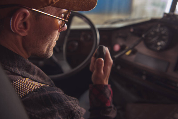 Two Way CB Radio Convoy Communication. Caucasian Trucker in His 40s Making Conversation Using Built In Truck Cabin Radio. Transportation and Communication Theme. - Foto, imagen