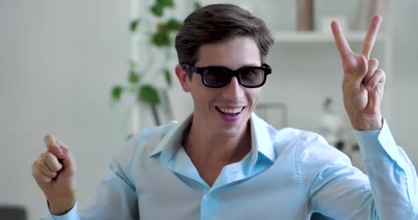 Portrait of cheerful funny Caucasian millennial magician man sitting at table wearing black glasses, playing with his hands, showing focus on his fingers, counting one two on his arms, smiling happy - Footage, Video