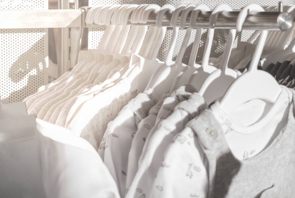 Fehér természetes ruhák gyerekeknek lógó állványon a boltban. Szerves anyagból készült babaruha. Absztrakt háttér. Szelektív fókusz - Fotó, kép