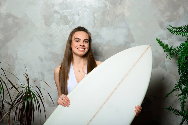 Gyönyörű fiatal nő pózol szörfdeszkával a stúdióban - Fotó, kép