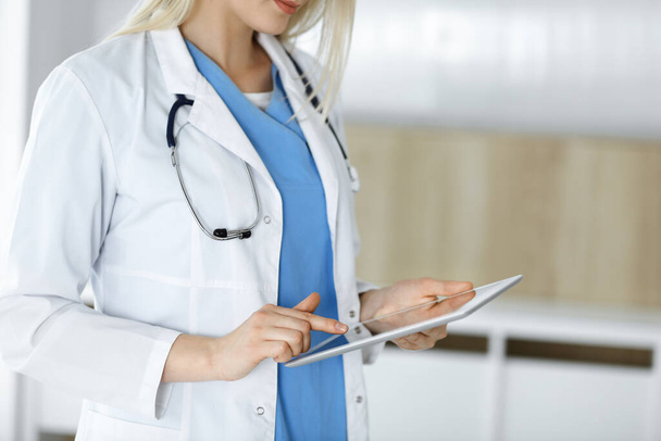 Unknown woman-doctor standing in clinic and using tablet pc, close-up. Data and best service in medicine and healthcare - Foto, Bild