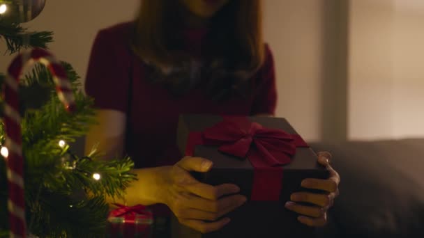 Młoda Azjatka o zabawy otwarcia X 'Mas obecne pudełko w pobliżu choinki ozdobione ozdobami w salonie w domu. Wesołych Świąt Bożego Narodzenia i Szczęśliwego Nowego Roku. - Materiał filmowy, wideo