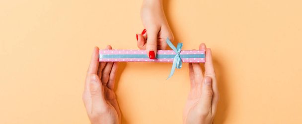 Top view of a man and a woman congratulating each other with a gift on colorful background. Surprise for a holiday concept. Close up. - Foto, Imagem
