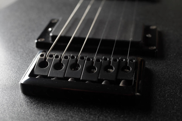 A close-up rusty bridge serves to secure the strings to an electric guitar. Black electric guitar in the dark. Selective focus. - Photo, Image
