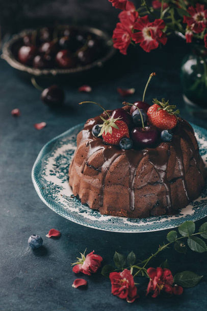 Zelfgemaakte chocoladetaart geglazuurd met chocolade en versierd met verse bessen, aardbeien, kersen en bosbessen - Foto, afbeelding