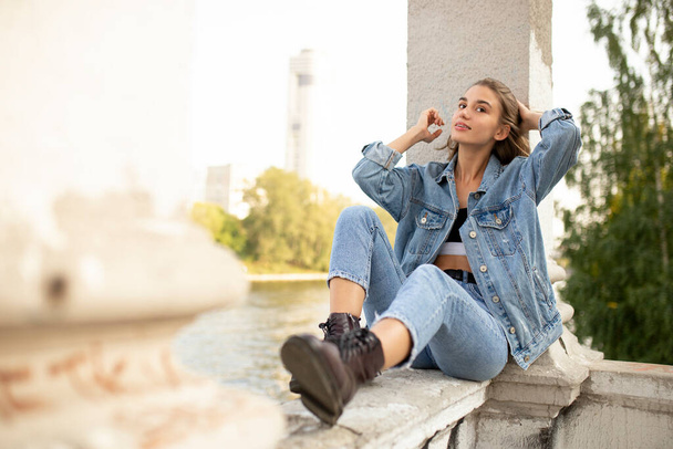 Portrait of a longing smiling teenage girl dressed in denim and boots, sitting outside. - Fotoğraf, Görsel