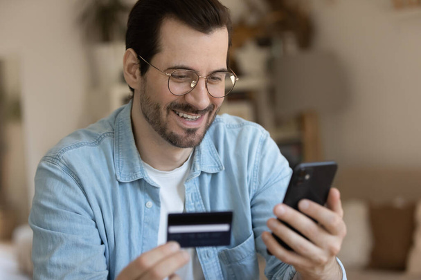 Young smiling man involved in online shopping in mobile app. - Zdjęcie, obraz
