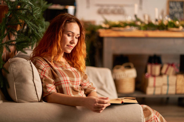 A cute girl is reading a book in a warm and cozy atmosphere. Relaxation and privacy concept. - Foto, Imagem