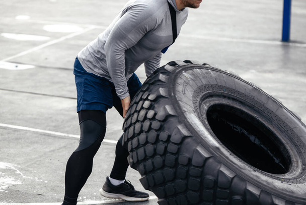 male athlete of Caucasian appearance, raises the steering wheel. strength training on an outdoor sports field. Does heavy exercises. favorite work. soft focus - Photo, Image