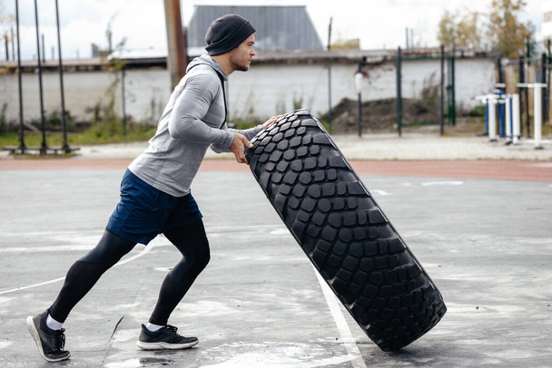 Sportlicher junger erwachsener kaukasischer Typ dreht das große Rad an der frischen Luft. Handgefertigte Sportgeräte - das Konzept einer gesunden Lebensweise - Foto, Bild